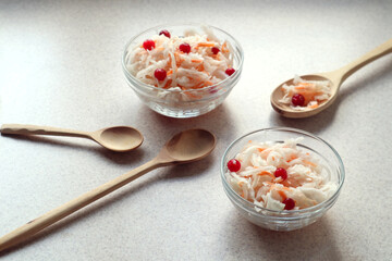 Sauerkraut with cranberry berries on a gray background, wooden spoons, side view-the concept of cooking delicious dishes from vitamin vegetables