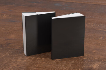 Two softcover or paperback vertical black mockup books standing on the wooden background. Blank front and back cover.