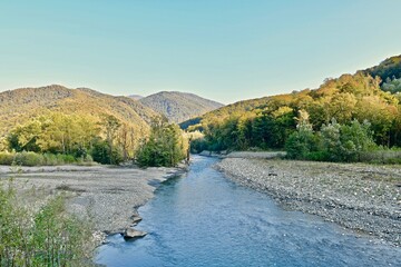 The bed of a rocky river among the mountain slopes covered with forest with dead wood