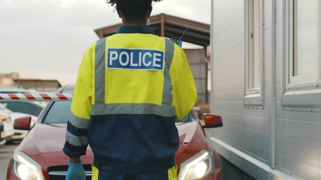 Back view of police officer in uniform with walkie talkie near car checkpoint