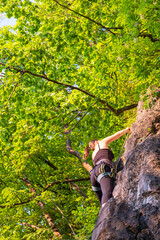 happy beautiful caucasian woman with long brown hair rock climbing, flexing her muscles on a sunny day in the mountains, strongly holding on to cliffs. Healthy outdoor sports and activities in nature