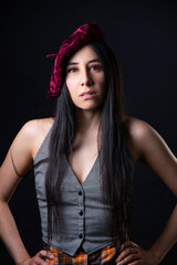 Fototapeta premium Fashion studio portrait of a young latin woman with long black hair wearing a red beret in a dark background