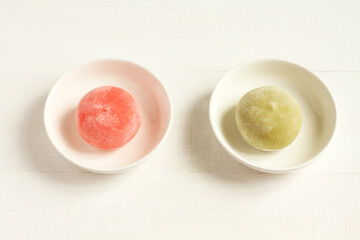 Two types of Japanese dessert mochi - pomegranate with honey and green matcha tea on a small white bowls on a white wooden table. Closeup