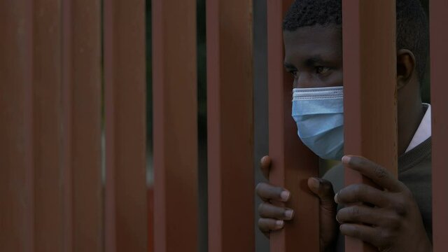 symbol of lack of freedom - black man wearing mask behind the bars of a gate 
