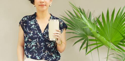 Bring your own cup, concept. A young beautiful woman stand holding a reusable insulated stainless tumbler glass to show awareness of 'Say no to plastic'. Daily waste, Coffee cup.