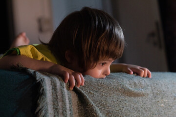 Niño sindrome down  mira curioso desde arriba de una cama hacia una luz