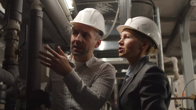 Engineers in hardhat standing near broken pipeline with warning light on having emergency