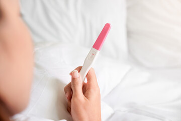 Unhappy young asian woman holding pregnancy test showing a negative result in her bedroom, wellness...
