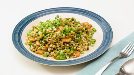 Pan-fried shrimp and blend of couscous, orzo, garbanzo beans, and red quinoa  served with green peas and green onion close up on a plate on white background