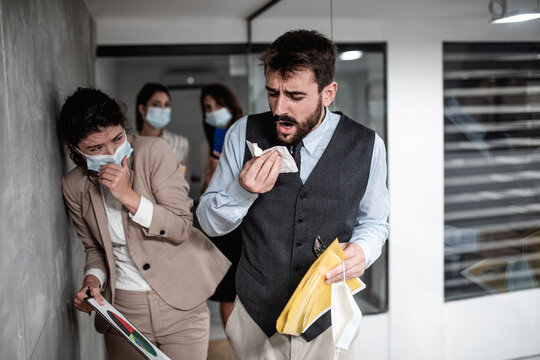 Group of business people with protective face masks against virus infection. One man is sick and he is coughing. Others are scared and trying to protect themselves. - Powered by Adobe