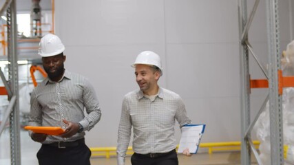 Warehouse workers in hardhat discussing inventory on digital tablet - Powered by Adobe