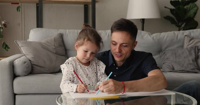 Loving dad spend weekend with cutie little daughter, family sit in living room at coffee table drawing pictures with colorful pencils enjoy hobby and pastime, leisure activity, kid development concept