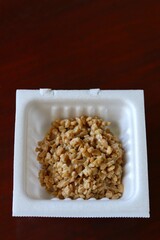 A close up shot of some finely chopped fermented soybeans in a small styrofoam packet. 