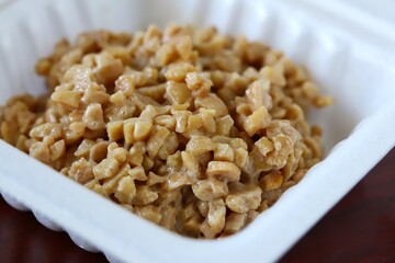 A close up shot of some finely chopped fermented soybeans in a small styrofoam packet. 
