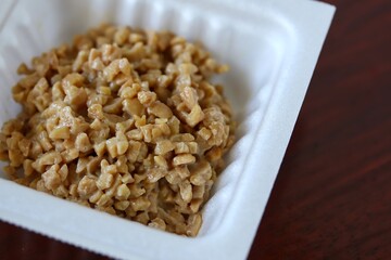 A close up shot of some finely chopped fermented soybeans in a small styrofoam packet. 