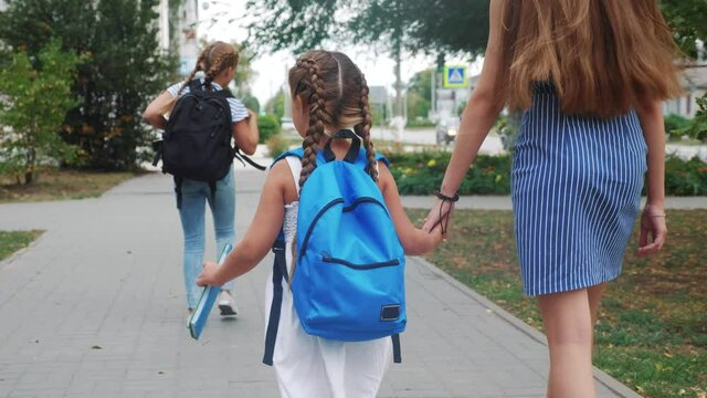 mom and daughter go to school. happy family school education concept. schoolgirl with mom go lifestyle hand in hand to school on footpath in the park. little girl with a briefcase time to study