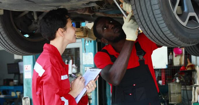 Black Male And Female trainee Mechanics Working Underneath Car Together Car maintenance and auto service garage.