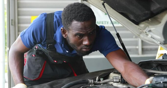 Black male mechanic repairs car in  garage. Car maintenance and auto service garage concept.
