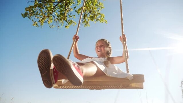 little girl kid swinging on a wooden swing on a tree in the park. happy family kid dream concept. little kid girl playing on fun wooden swing on tree dream concept in park