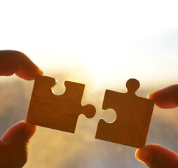 2 two hands trying to connect couple puzzle piece with sunset background. Jigsaw alone wooden...
