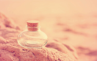 A beautiful empty pot-bellied glass bottle of an unusual shape stands on the beach stones close-up in the pink rays of the sunset. Wallpaper postcard welness banner. Free space for text
