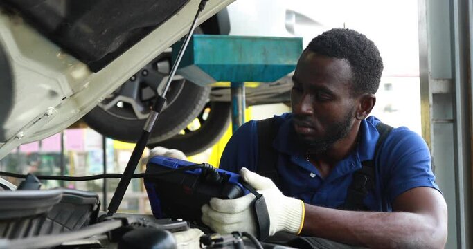 Professional car mechanic repair service and checking car engine by Diagnostics Software computer. Expertise mechanic working in automobile repair garage.