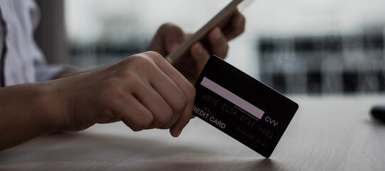 An Asian woman holds a black credit card and is shopping online on a cell phone. She is in the office.