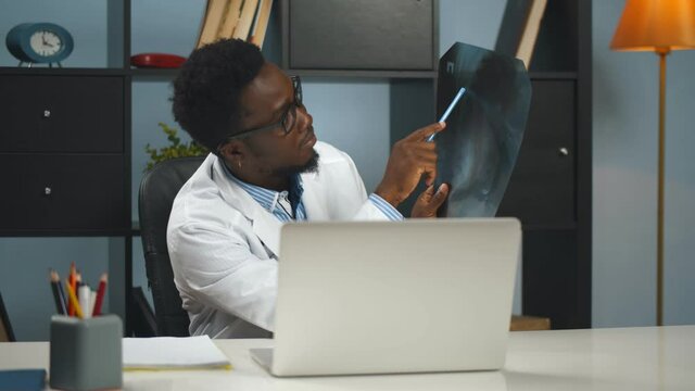 Afro-american male doctor working from home and showing x-ray to patient online