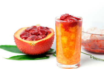 Gac juice in a glass with gac fruit and green leaves on a white background