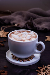 Cup of coffee with marshmallows and wooden snowflakes on dark wooden table. Winter concept, dark mood photo.