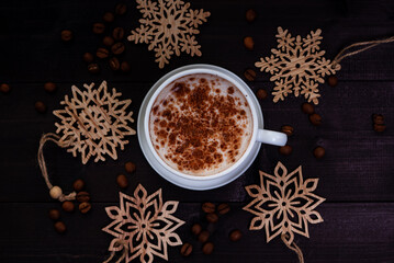 Obraz na płótnie Canvas Cup of coffee and wooden snowflakes on dark wooden table, top view. Creative flat lay winter arrangement.