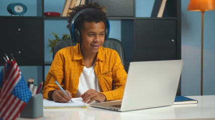 Preteen afro schoolboy doing homework with laptop at home.