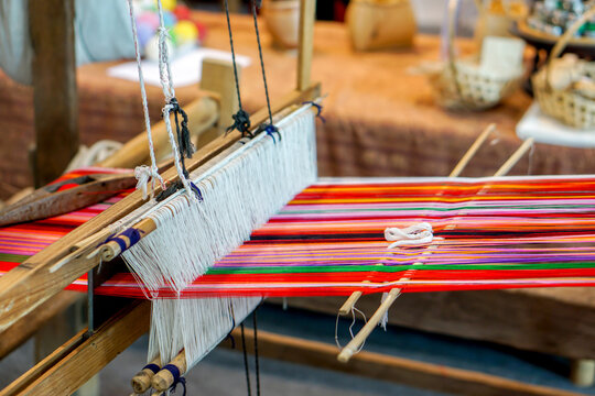 Closeup and crop colorful yarns with ancient wooden weaving machine on blurred background.