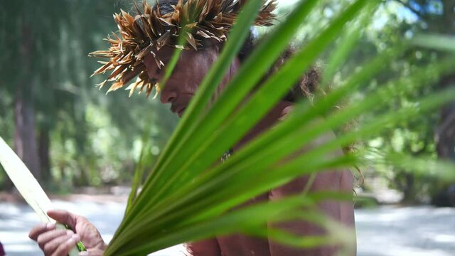 Joyful indigenous man with tattoos in Bora Bora Tahiti island, making traditional Tahitian hat from palm leafs. Exotic travel vacation getaway, romantic honeymoon destination.