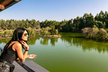Caucasian woman on viewpoint platform looks right with green nature and lake in the background. Blank space image. Dendrological park.Georgia.