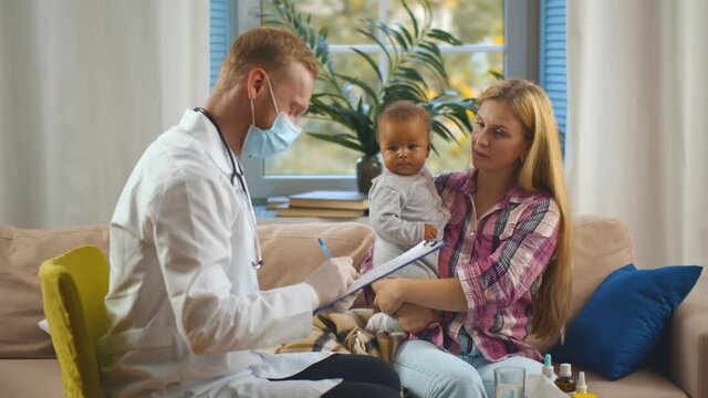 Caucasian woman with adopted mixed race baby consulting pediatrician at home