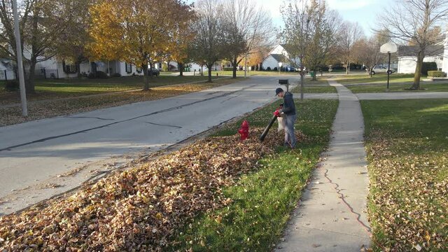 Aerial view of a man cleaning the autumn leaves with yard leaf vacuum on a suburban street. American suburban neighborhood. Residential single family houses.4K