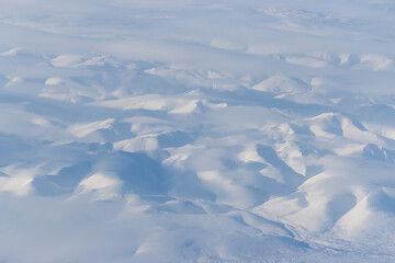 Fototapeta premium Aerial view of snow-capped mountains and clouds. Winter snowy mountain landscape. Icheghem Range, Kolyma Mountains. Koryak Okrug (Koryakia), Kamchatka Krai, Siberia, Far East Russia. Great background.