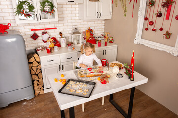 Little girl prepares Christmas cookies in the kitchen decorated for the holiday