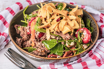 A serving of Lamb Salad in a round bowl with red and white striped napkin