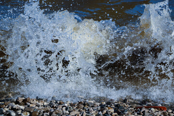 waves run onto the shore and crash against the rocks, creating many splashes and splashes near the shore. river surf in stormy weather near a stone pebble coast with foamy splashing waves.