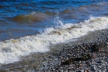 waves run onto the shore and crash against the rocks, creating many splashes and splashes near the shore. river surf in stormy weather near a stone pebble coast with foamy splashing waves.
