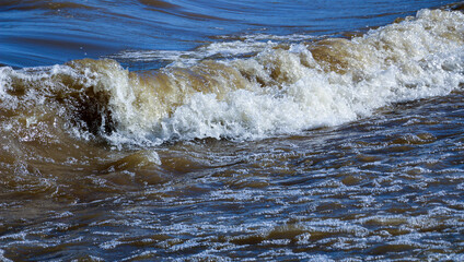 waves run onto the shore and crash against the rocks, creating many splashes and splashes near the shore. river surf in stormy weather near a stone pebble coast with foamy splashing waves.