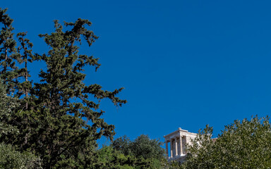 distant view of Athena Nike ancient temple between trees and clear blue sky, Athens Greece