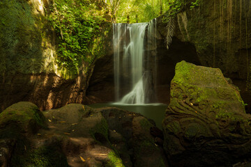 Waterfall landscape. Beautiful hidden waterfall in tropical rainforest. Foreground with big stones. Slow shutter speed, motion photography. Suwat waterfall, Bali, Indonesia