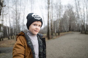 a boy looks at the camera with a sly look, outdoors in winter clothes, a black hat and a mustard jacket, a small handsome man