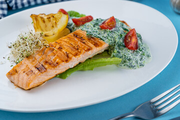 Grilled salmon steak. A piece of red fish on a white plate and a blue background on the table. Fish food with sauce, tomatoes, lemon. Restaurant menu. Grill fried.