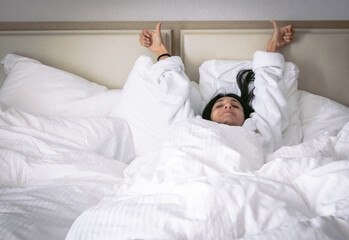 Obraz na płótnie Canvas Happy woman shows thumbs up sign laying in big bed with many pillows