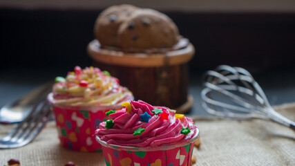 Cupcakes with cute colourful tiny topping in different shapes and Chocolate chips cookies on the black background, text and copy space available.