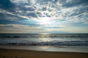 Blue ocean beach sunset with blue cloudy sky and sun rays.